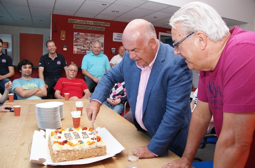 KNRM-Huizen voorzitter Fons Hertog snijdt de jubileumtaart aan, onder toeziend oog van de bemanning 